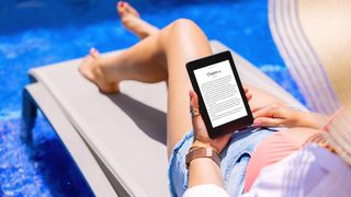 Woman holding e-reader device and reading e-book by the pool