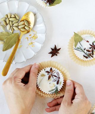 A female with unpolished nails making DIY wax firestarters with melted leftover wax, using whole star anise and cinnamon