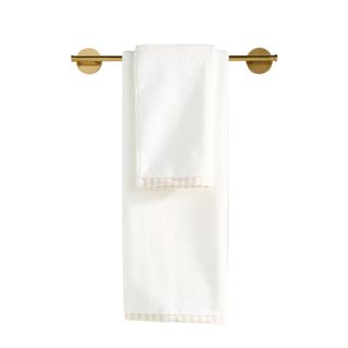 A folded white towel with a beige striped hem hanging from a brushed gold towel bar