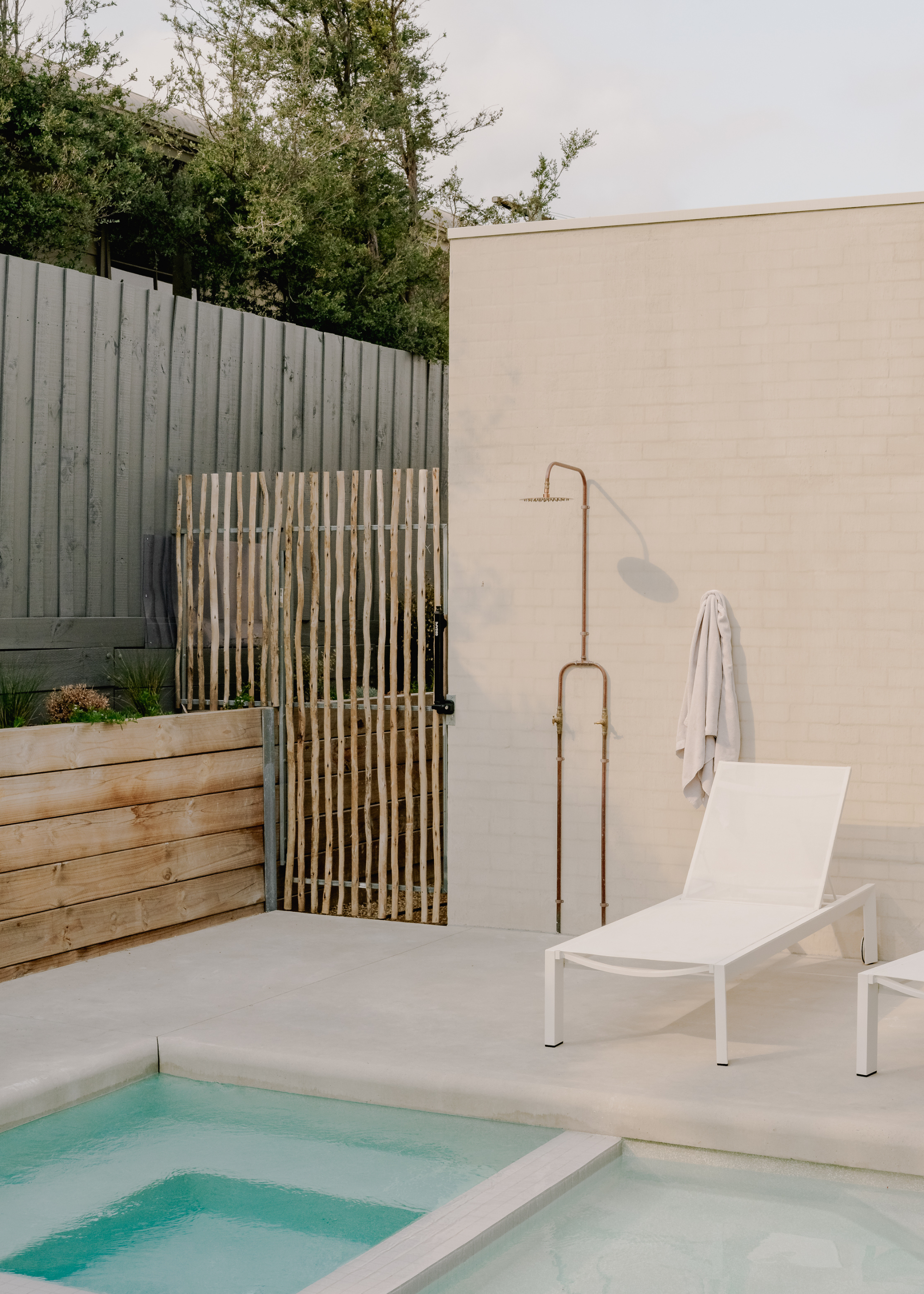 A backyard pool with an outdoor shower and a gray fence