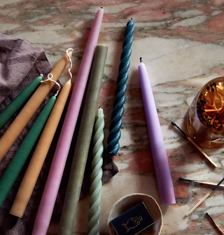 tapered candles in a mix of colors and styles laid on a flat surface with matches alongside