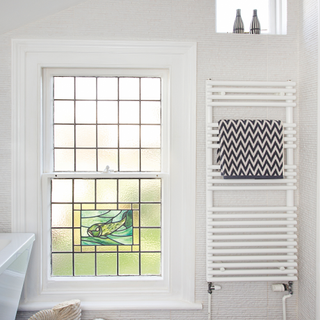 Stained glass bathroom window, heated towel rail with dark grey chevron towel, marine fossil ornament.