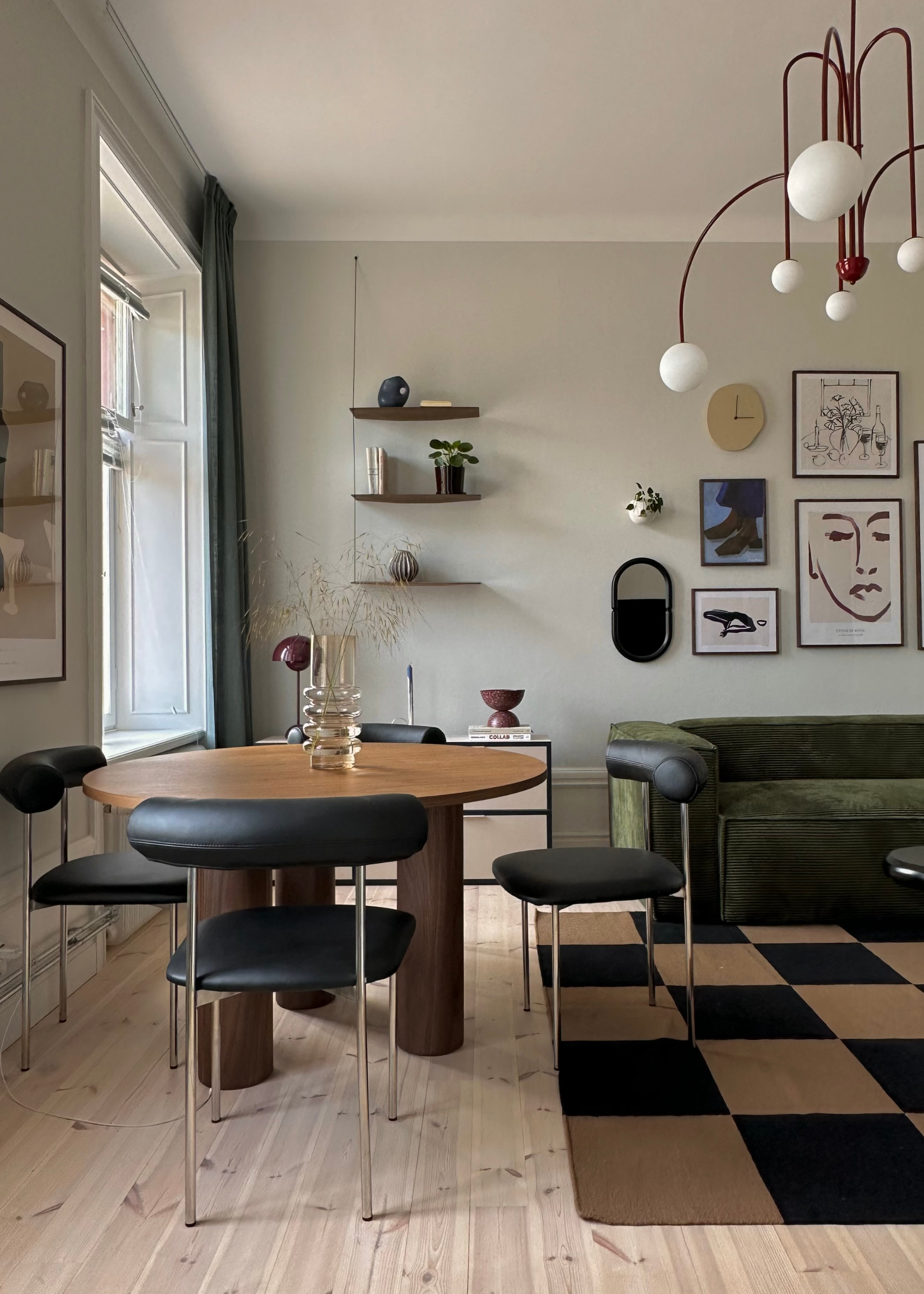 A living room with a wood dining table and black dining seats, checkerboard rug, green sofa and a red ceiling light