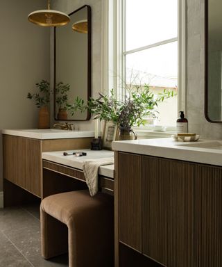 Organic bathroom with marble countertop and brown fluted cabinets, plants and pendant light