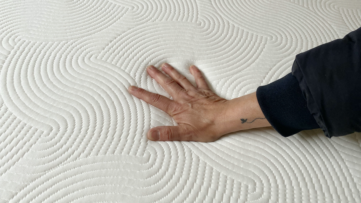 Our lead reviewer, who is wearing a black jumper, places her hand on top of the Brook + Wilde Lux Mattress to see if it remains cool to the touch during a temperature regulation test