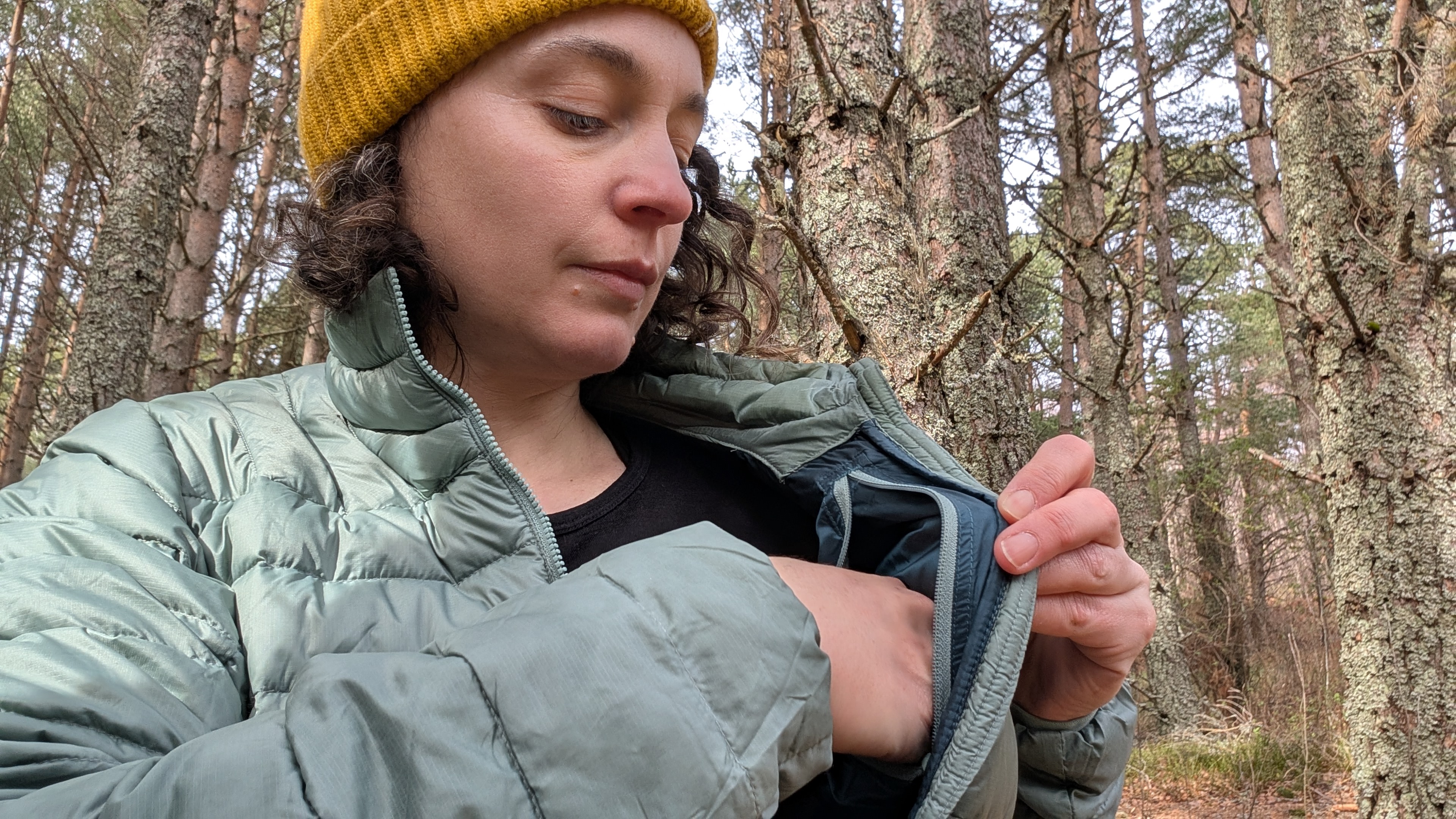 A woman opening the inner pocket on her green down jacket