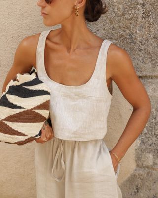 Emily wears linen tank and linen pants with a patterned bag in her hands.