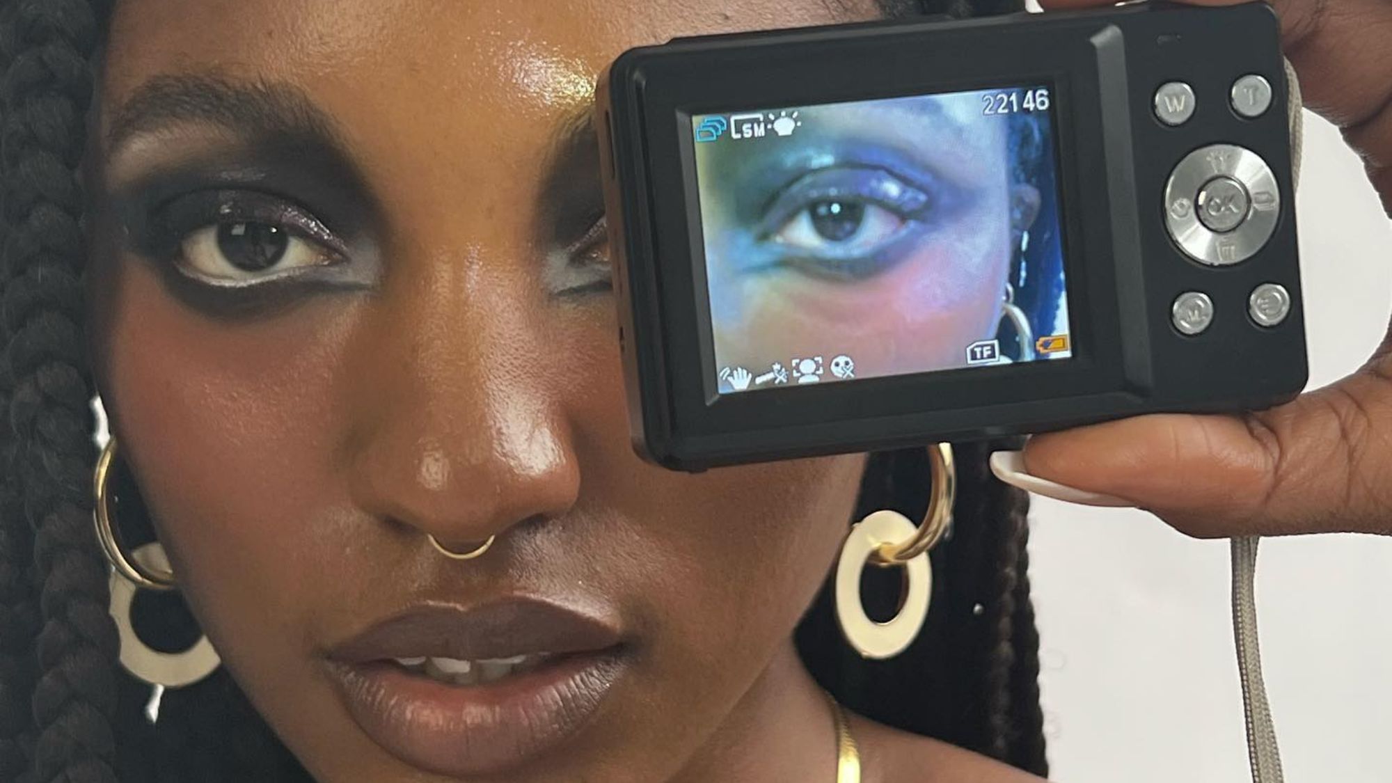 An image of a woman with heavy eye makeup and a digital camera in front of one eye.