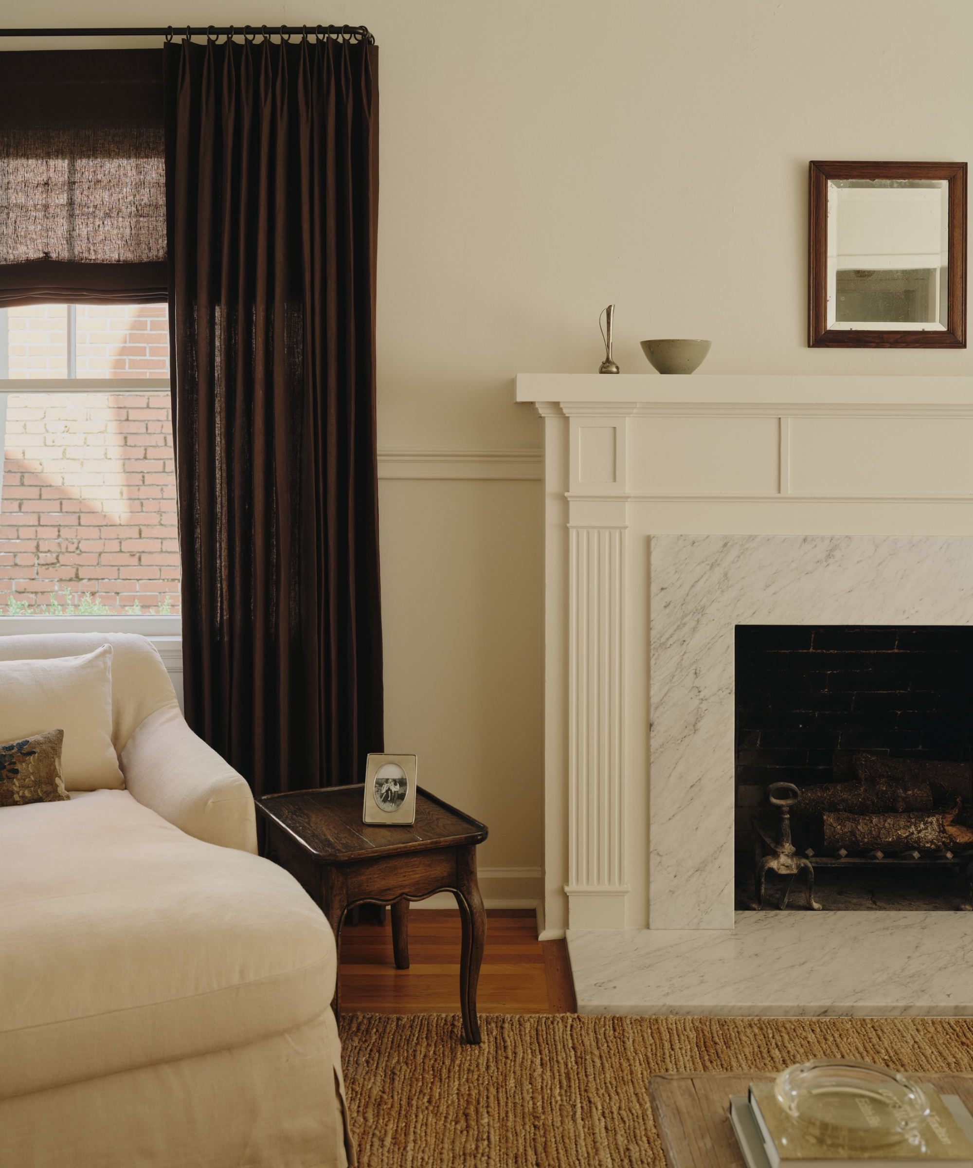 Minimalist living room featuring a mantel topped with decorative objects, a rectangular wall mirror, and a set of brown drapes.