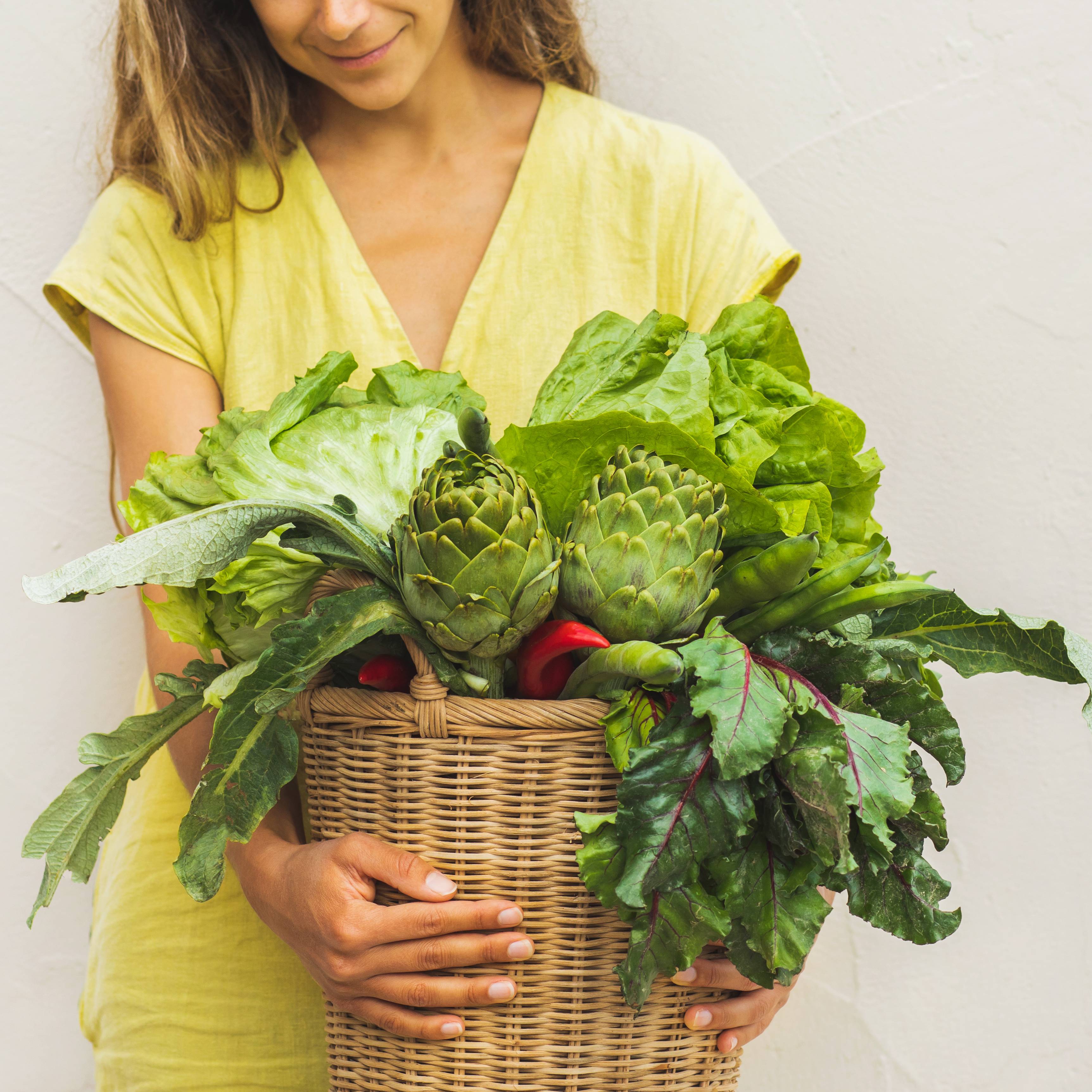 A smiling woman holds a basket of fresh vegetables