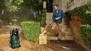 A man using a Karcher pressure washer to clean a stone staircase