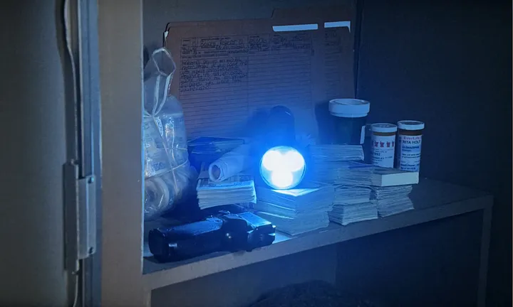 A photograph of the inside of a cabinet with various items on a shelf, including a lit torch aimed right at the lens.