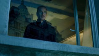Michael Fassbender's unnamed protagonist stares menacingly out of a window in The Killer