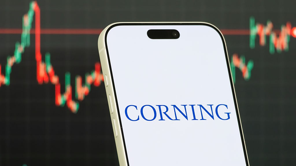 Corning logo on a smartphone with a blurred stock chart in the background