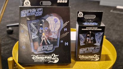 Two pins contained in carboard packaging on a golden side table