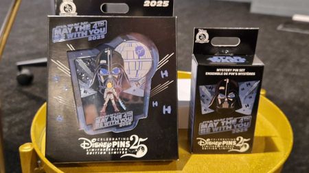 Two pins contained in carboard packaging on a golden side table