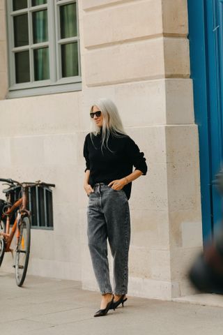 A woman at Paris Fashion Week wearing gray barrel wide-leg jeans, a black turtleneck, and black slingback heels