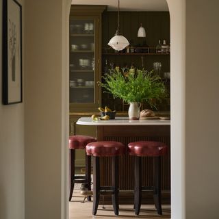 View into kitchen with olive cabinets and mulberry stools