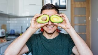 Smiling man holding avocado halves over eyes