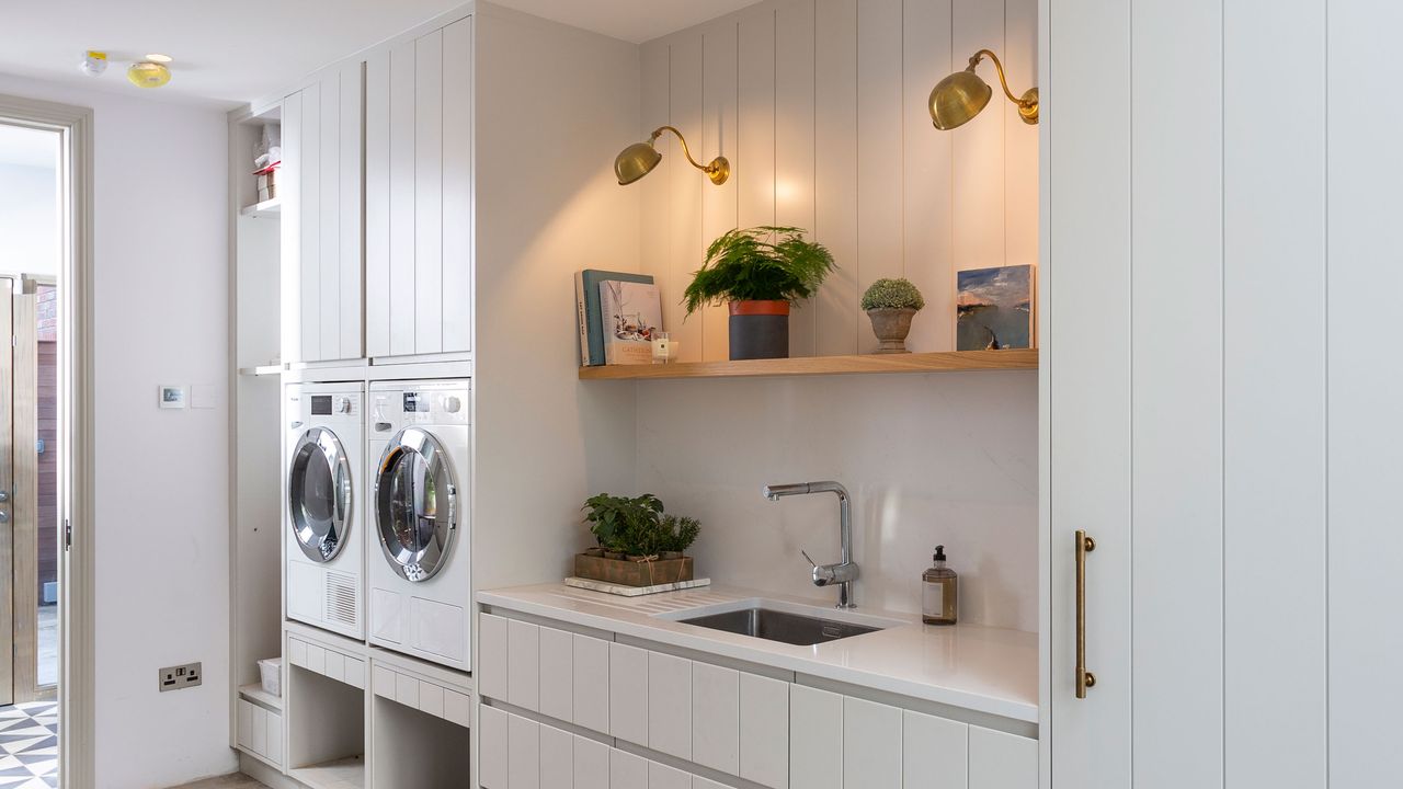 utility room with wall lights switched on. In this laundry room with washing machine has been integrated into paneled walls. There is also a wink and open shelving. 