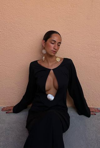 Shell jewelry trend shown on a woman wearing a black maxi dress with a keyhole cutout and shell hoop earrings.