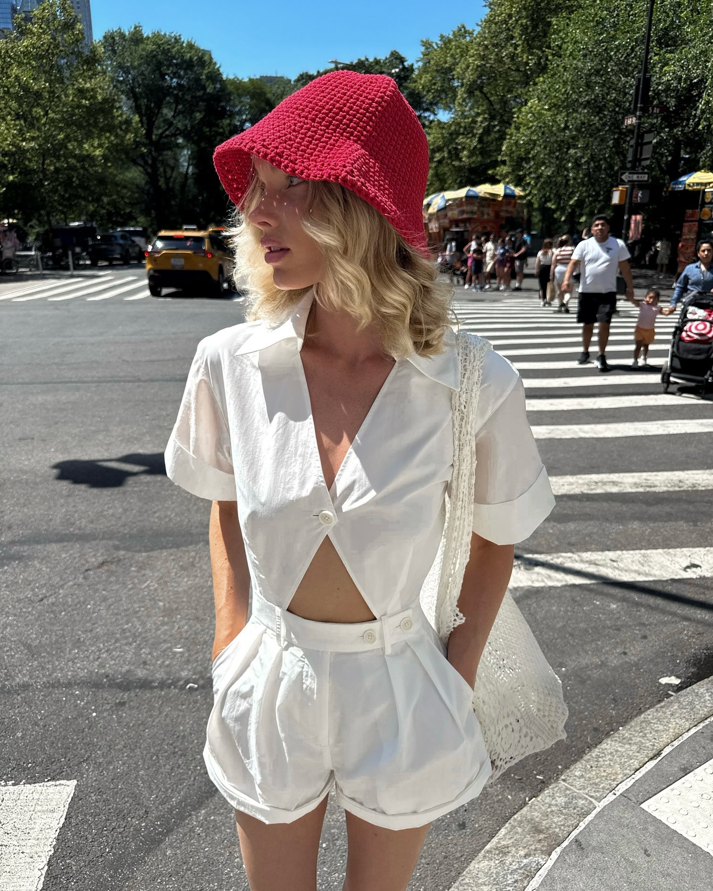 Model Elsa Hosk wears a red crochet bucket hat, a white linen set and is carrying a crochet white bag. She is stood in a crosswalk in New York in a recent image from her Instagram.