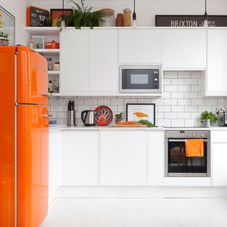 kitchen area with wooden floor and orange fridge and white cabinets