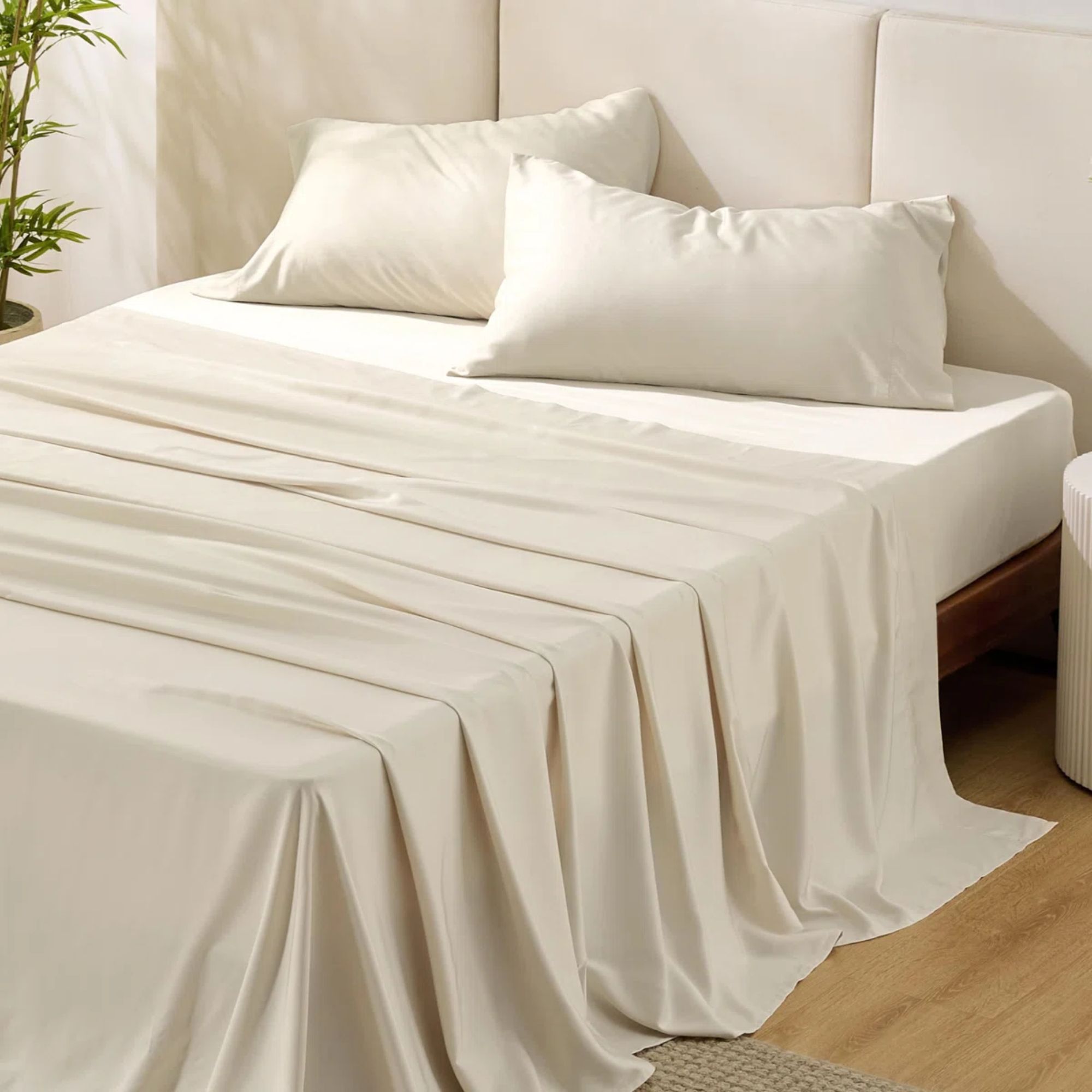 Bedsure white cooling bedsheets pictured on a white bed in a white room with light wood flooring beside a large houseplant and white concertina bedside table