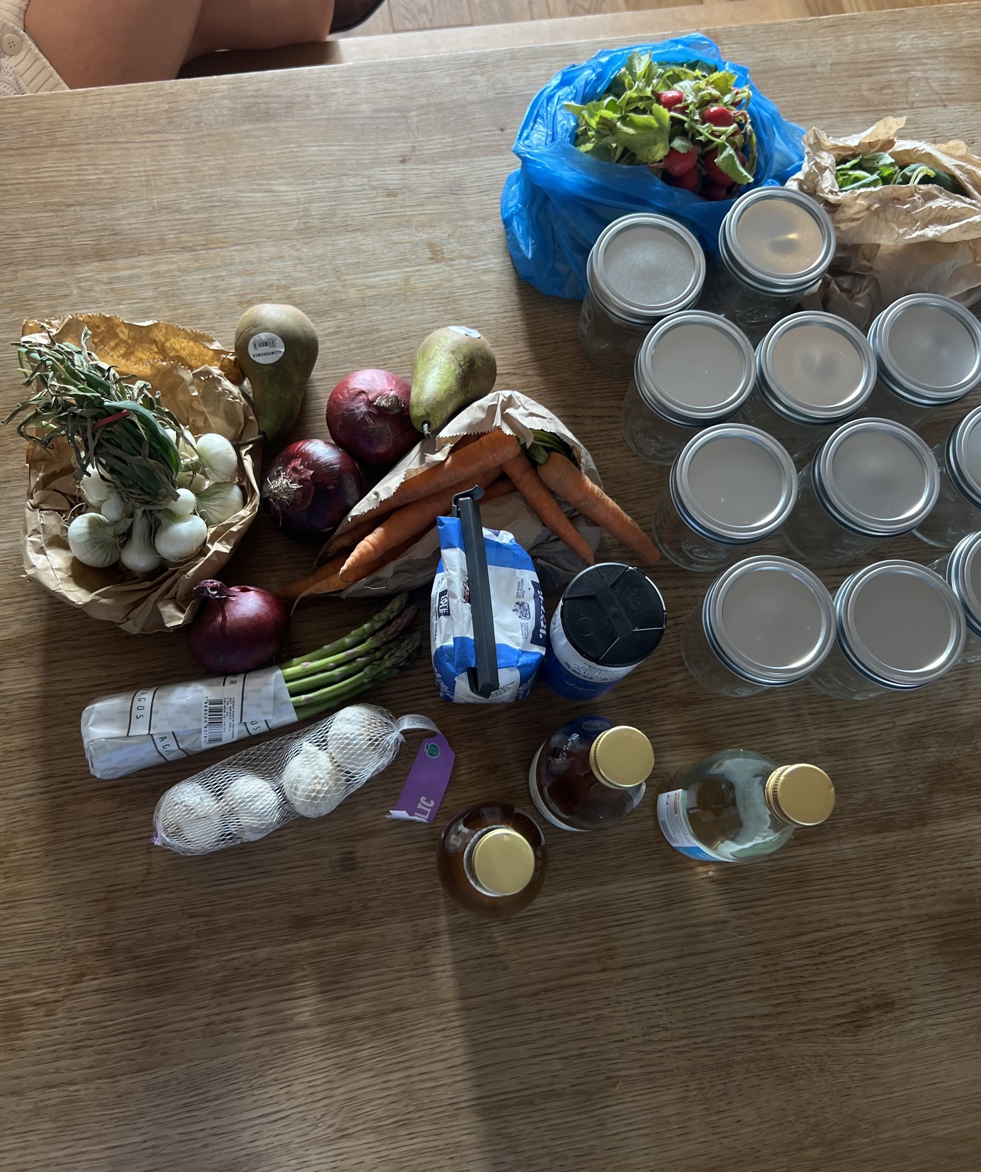 Image of a table from above that is covered in different pickling supplies. There are several jars, different types of vegetables, and bottles of vinegar.