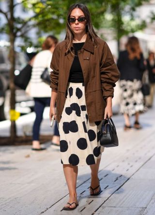 A NYFW guest wearing a brown coat with a polka dot skirt and black top.