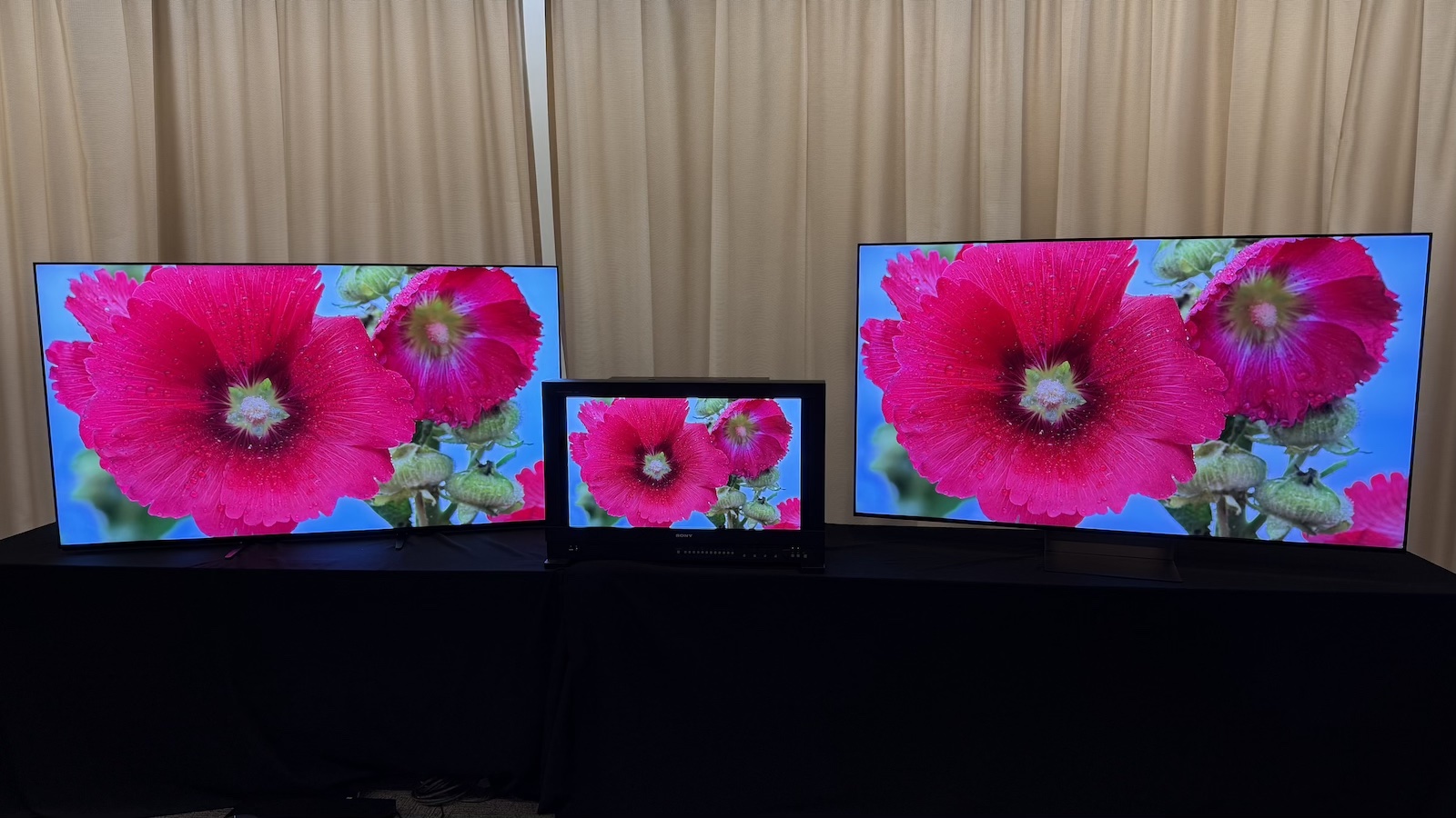 The Sony Bravia 9 II and Bravia 9 TVs, and the Sony BVM-HX3110 mastering monitor, photographed on a black desk, with Sony demo footage on the screens