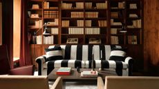 A dark wood living room with floor to ceiling bookshelves. A black and white stripped couch in front of them. 