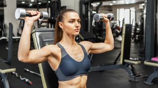 a photo of a woman doing a shoulder press with dumbbells