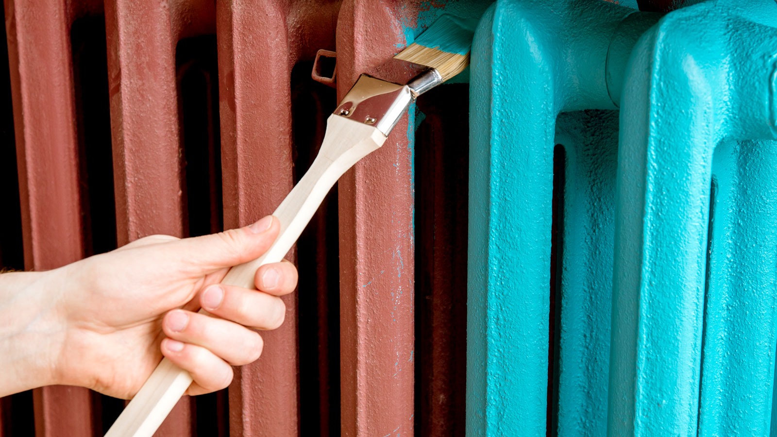 Hand holding long handled paintbrush painting primed column radiator teal