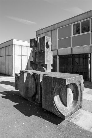 A black & white photo of a concrete sculpture. Concrete block with circular motifs on the surface.