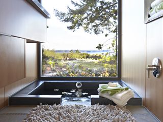 A large square spa-like bath with a huge clear vista window with a great view