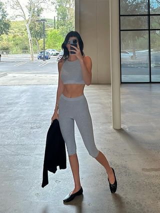 Kendall Jenner wearing a gray Alo sports bra with matching capri leggings and black ballet flats.