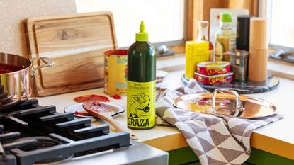 kitchen bench with graza olive oil and other condiments with tea towel and cutting board