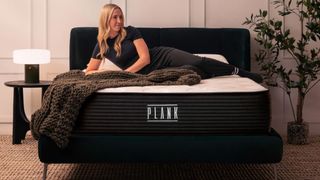A woman lies on the Plank Firm Luxe Zoned mattress in a well lit bedroom