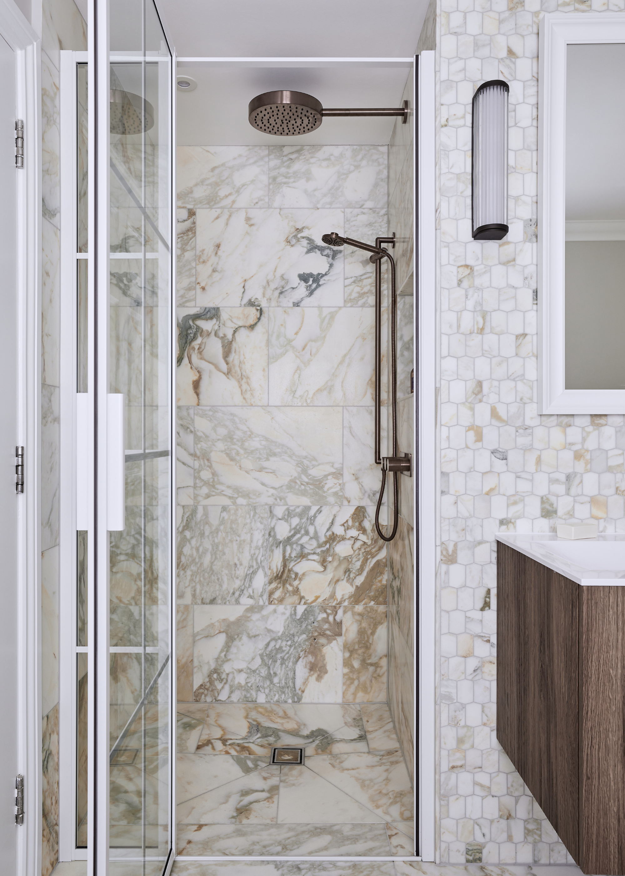 a shower enclosure with large format marble tiles, the rest of the bathroom is covered in smaller tiles of the same marble