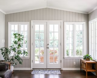 Large and open living room den sun room with windows on two sides and lots of natural light flowing in. There is a window seat on one side and a leather couch and plant on the other