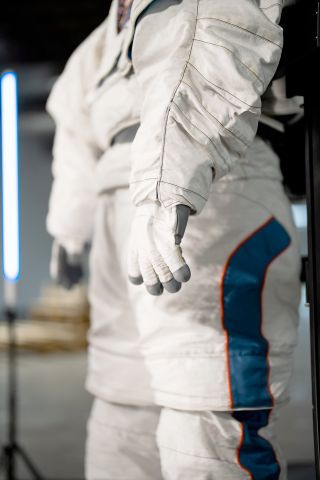 closeup of a white spacesuit glove, with the rest of the suit visible in the background.
