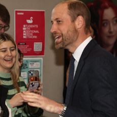 Prince William wearing a blue suit and tie talking to a crowd students and laughing 