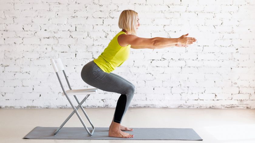 woman doing squat next to chair