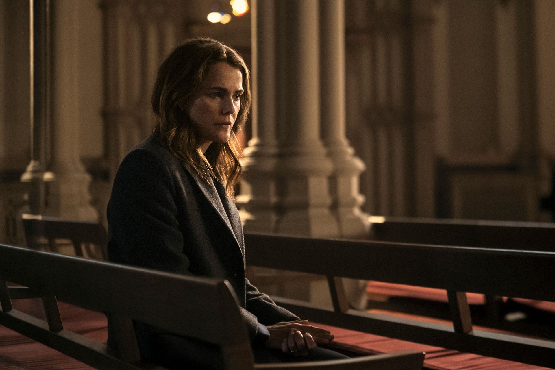 Keri Russell as Kate Wyler, sitting on a pew in a cathedral, in episode 401 of The Diplomat.