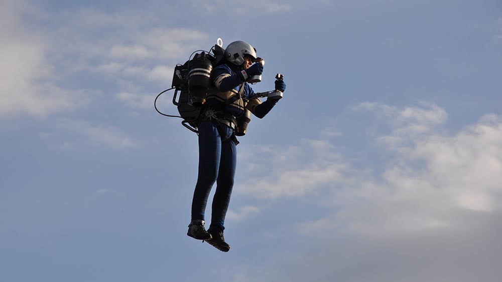 A person wearing a jetpack and a helmet hovers in the air.