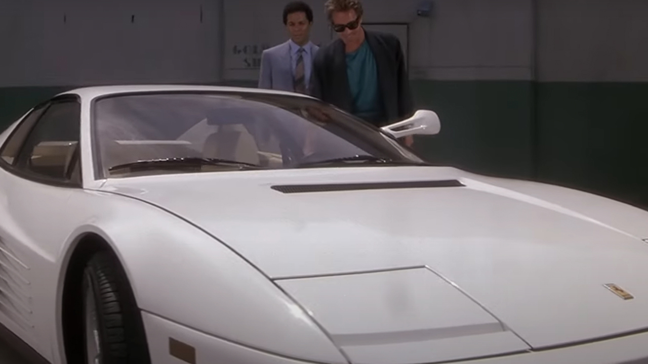 A white Ferrari from the hood looking back, with two people standing behind it.