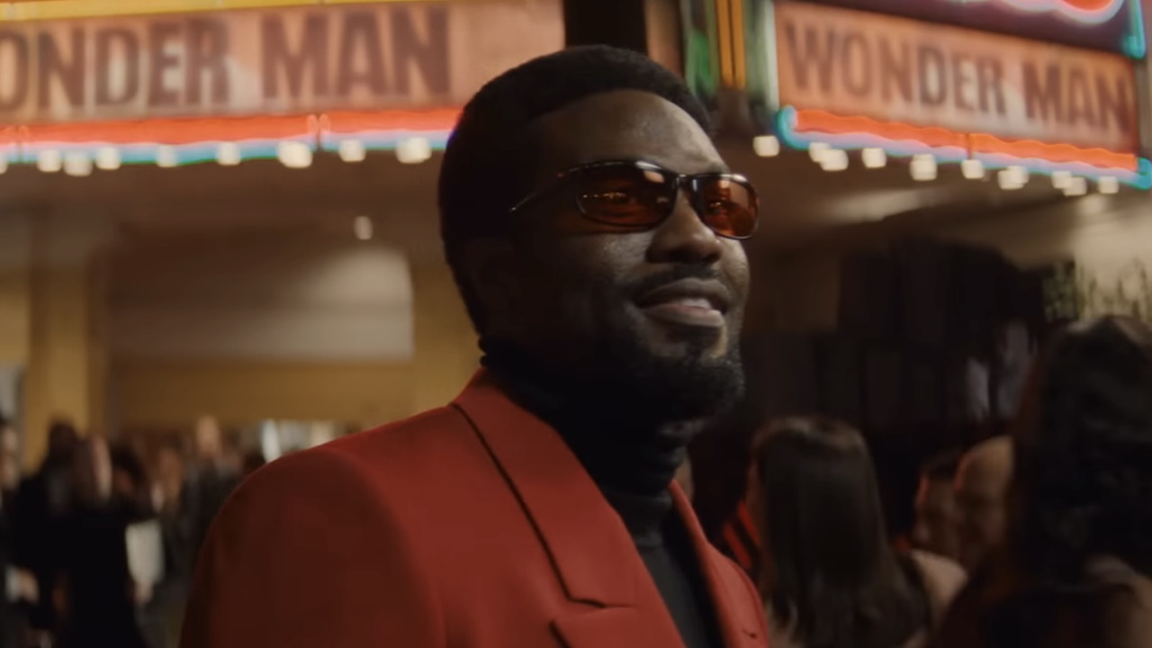 Simon Williams in sunglesses and red suit outside theater with Wonder Man on marquee in Wonder Man Season 1