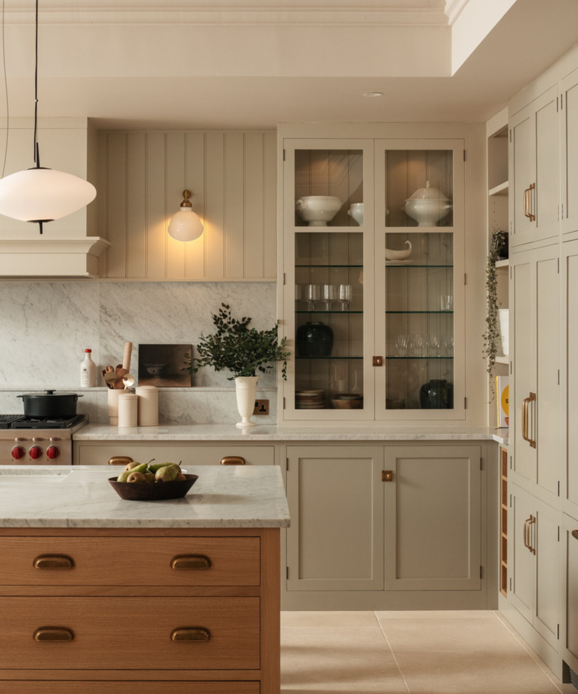 The corner of a green kitchen with glazed cabinets and a mixed material backsplash