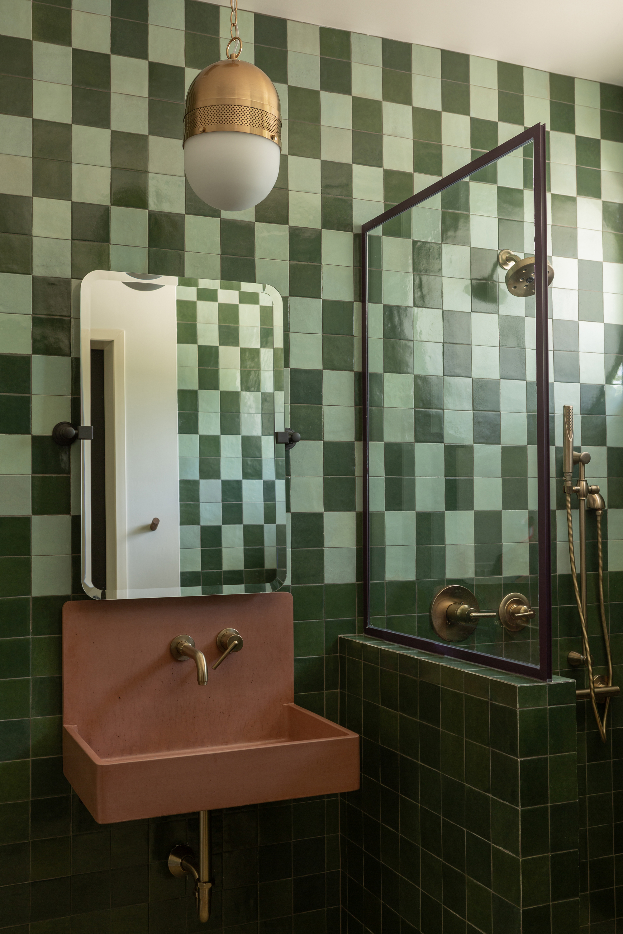 green bathroom with two-tone checkered wall tiles, terracotta colored sink, ceiling pendant light and shower with niche wall and gold taps